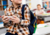 Child with smartphone and backpack sitting in classroom