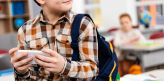 Child with smartphone and backpack sitting in classroom