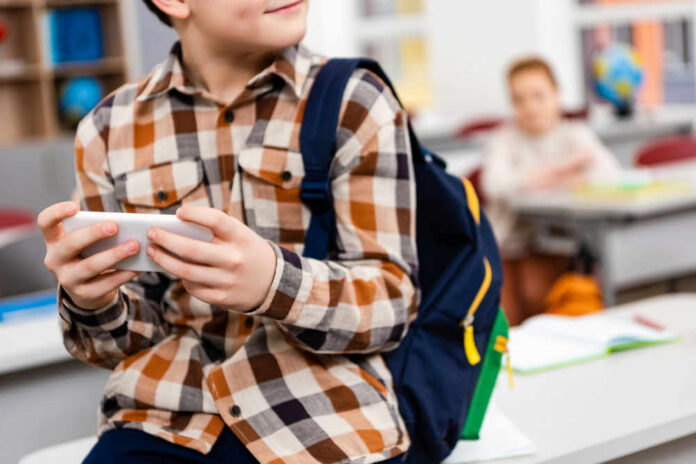 Child with smartphone and backpack sitting in classroom