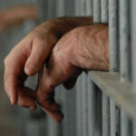 Hands resting on jail cell bars.