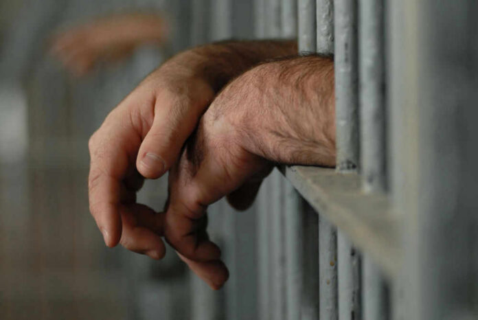 Hands resting on jail cell bars.