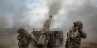 Soldiers fire a field howitzer as smoke and dust rise around them