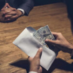 Hands placing cash into an envelope at a wooden table
