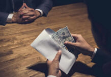 $38M Daycare Scam Explodes In Brooklyn Hands placing cash into an envelope at a wooden table