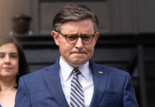 Man in blue suit with glasses looks down thoughtfully