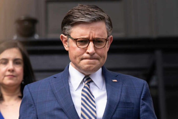 Man in blue suit with glasses looks down thoughtfully