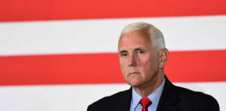 man in suit with red tie in front of red and white stripes