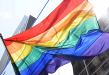 Utility Deals Now Identity-Tagged A vibrant rainbow flag waving against a city backdrop