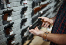 Colorado’s Gun Files — No Judge, No Limits? Person holding a handgun in a gun shop with various firearms displayed on the wall