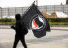 Person in black hoodie carrying a large black flag while walking on a street