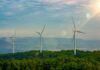 Three wind turbines on a green hillside under a cloudy sky