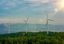 Three wind turbines on a green hillside under a cloudy sky