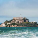 Alligator Alcatraz Blinked at First Big Gust View of Alcatraz Island with buildings and lighthouse surrounded by water