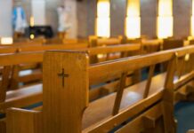Worship Turns Tactical—Churches Arm Up Wooden church pew with carved cross in a sunlit sanctuary