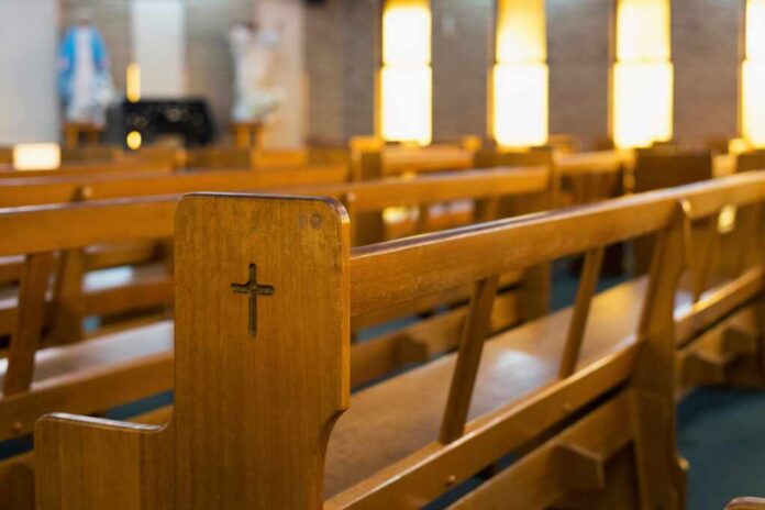 Wooden,Church,Pews,With,A,Carved,Cross,In,A,Softly Wooden church pew with carved cross in a sunlit sanctuary