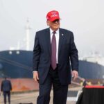 G7 Laughs—Then Things Get Tense A man in a suit wearing a red cap stands near a ship at a harbor