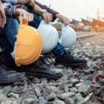 Railway workers sitting on track ballast holding hard hats