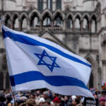 Israeli Power Play: U.S. Takes The Hits Israeli flag at a crowded outdoor event.