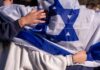 Wartime Spy Flip Inside Israel’s Ranks People holding an Israeli flag together, showcasing unity and cultural pride