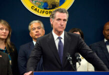 Newsom World Rocked By Co-Conspirator Person speaks at podium with California seal behind.