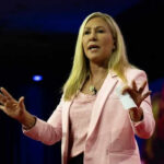 Woman speaking on stage wearing pink blazer
