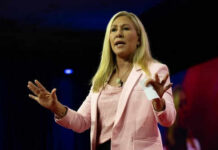 America-First Mutiny: Greene Ditches GOP Woman speaking on stage wearing pink blazer