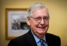 DC Ambulance, Then Silence—Where’s McConnell? Smiling man in suit with round glasses indoors.