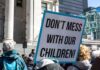 Strict Liability Tsunami Targets Gender Clinics protest sign held in a crowd outside a government building