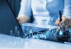 Businessperson analyzing stock data on tablet beside laptop