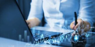 Businessperson analyzing stock data on tablet beside laptop