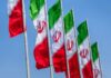 Strikes Near Hospital? Proof Or Propaganda? Multiple Iranian flags waving against a clear blue sky