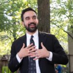 Socialist Shock: Wall Street Blinks? Man in suit speaking with hands on chest outdoors