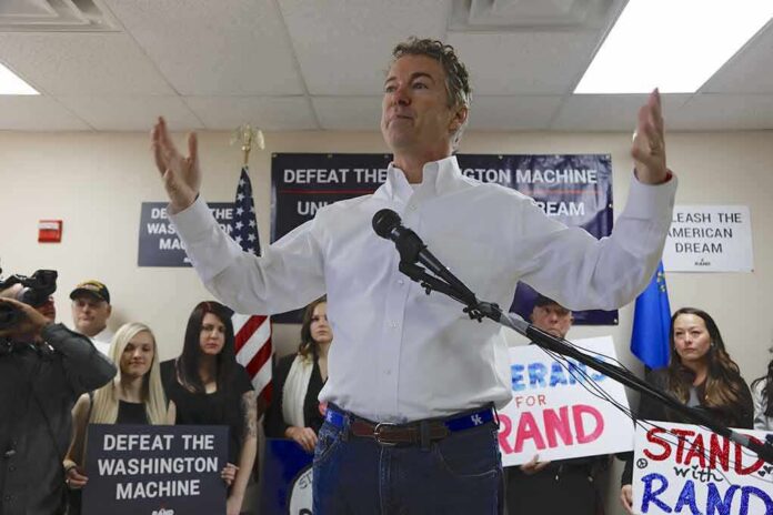 man in white shirt speaking at a rally with supporters and signs behind him