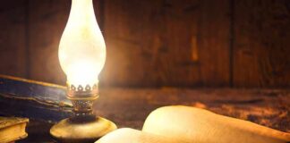 Open antique book beside a glowing oil lamp