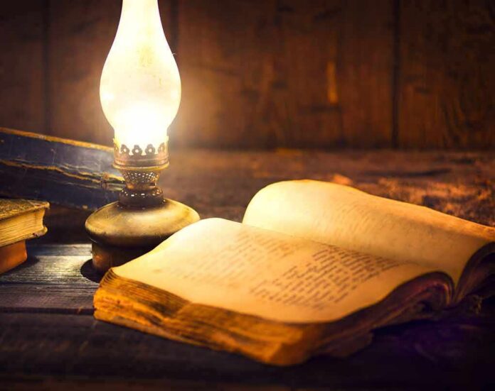 shutterstock_562045069 Open antique book beside a glowing oil lamp