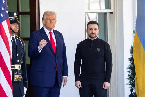 Two men standing outdoors near flags and doorway