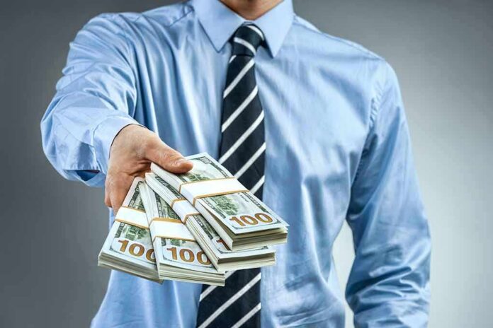 shutterstock_1008204853 Person in business attire offering bundles of US dollar bills