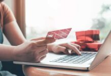 Person holding credit card while typing on laptop