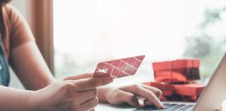 Person holding credit card while typing on laptop