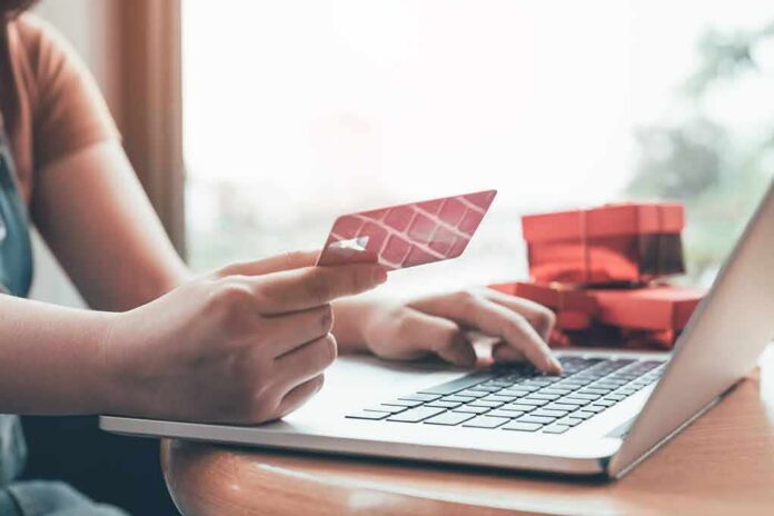 Person holding credit card while typing on laptop