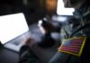 Soldier with U.S. flag patch using a laptop in a dim room