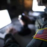 Soldier with U.S. flag patch using a laptop in a dim room