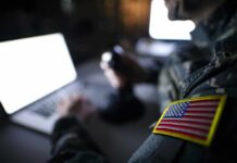 Soldier with U.S. flag patch using a laptop in a dim room