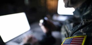 Soldier with U.S. flag patch using a laptop in a dim room
