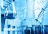 Drug Titans Plot $400B Dominance Scientist holding a flask with blue liquid and pipette over test tubes