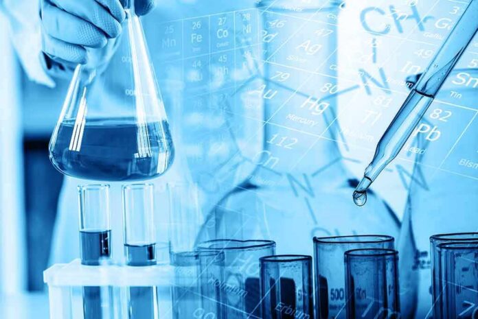 shutterstock_1453648280 Scientist holding a flask with blue liquid and pipette over test tubes