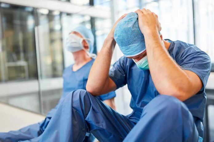Two exhausted healthcare workers in scrubs sit on the floor