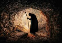 A silhouette of a mysterious figure with a walking stick standing in a dark cave surrounded by overgrown vegetation