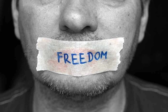 shutterstock_187662866 A mans mouth is covered with a piece of tape that has the word FREEDOM written on it