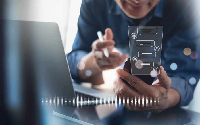 shutterstock_2152122605 Person using smartphone with chat bubbles and laptop
